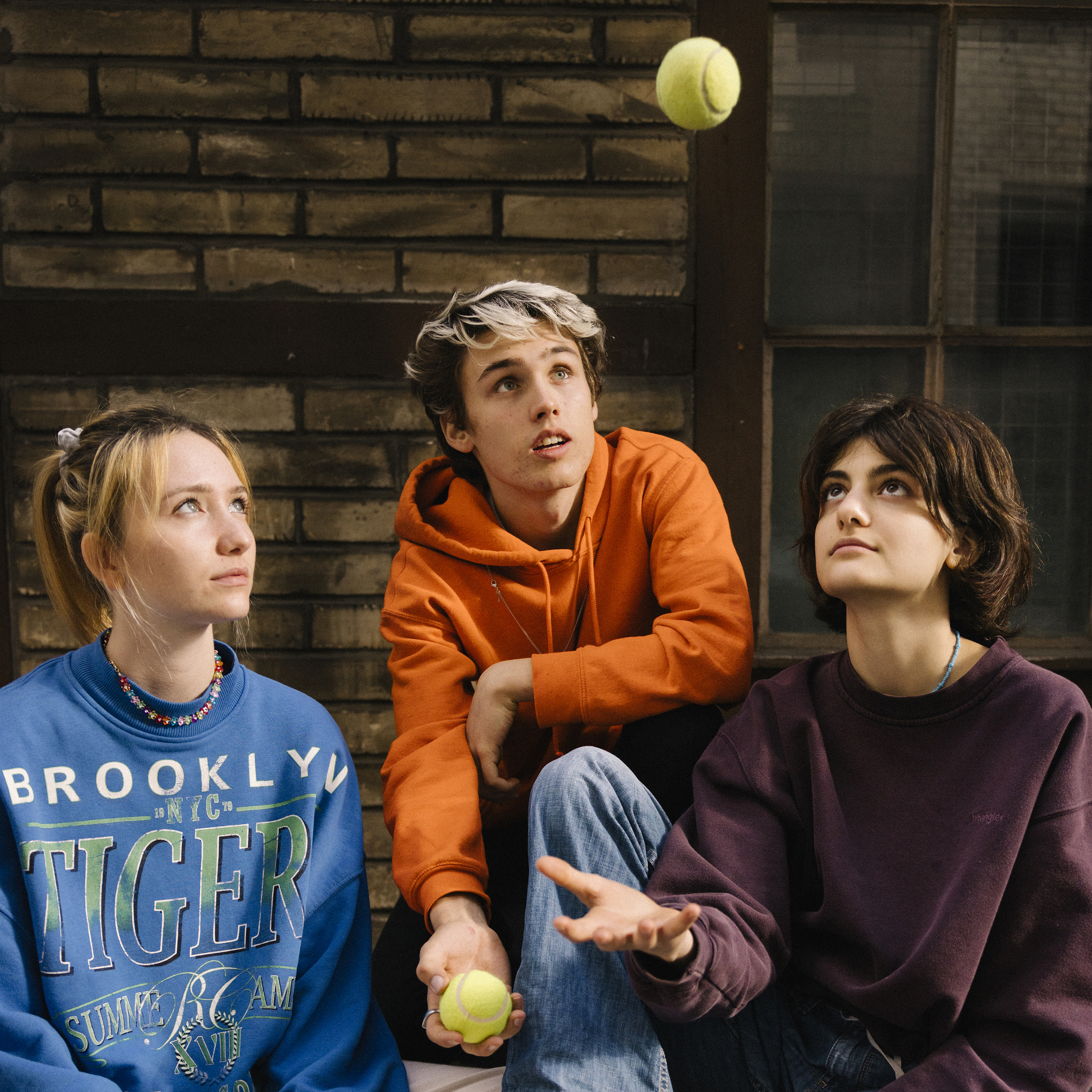 Three teenagers stare focused at a tennis ball thrown into the air.