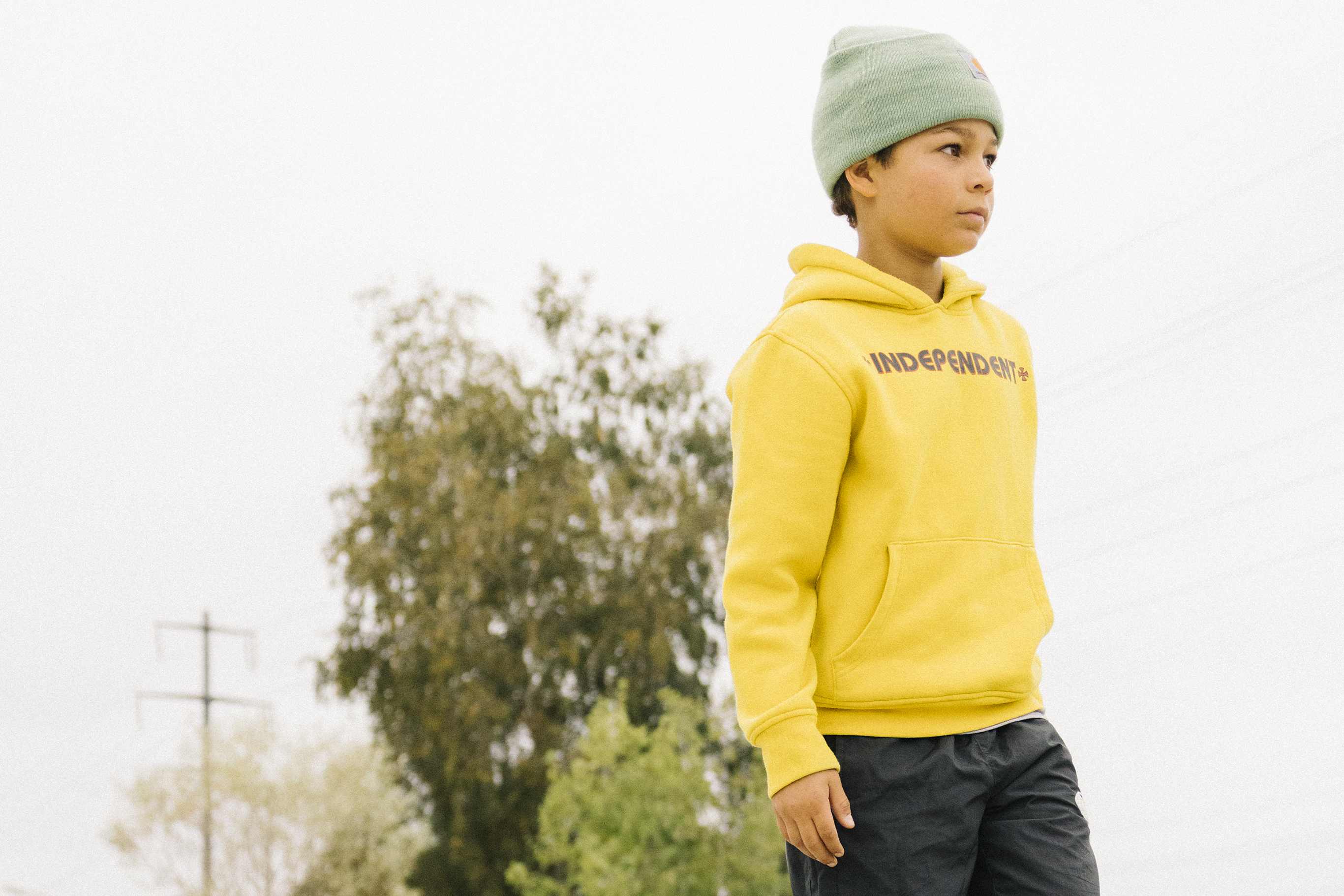 Un adolescent debout sur son skateboard se tient sur une barre de grind et regarde au loin, sûr de lui.