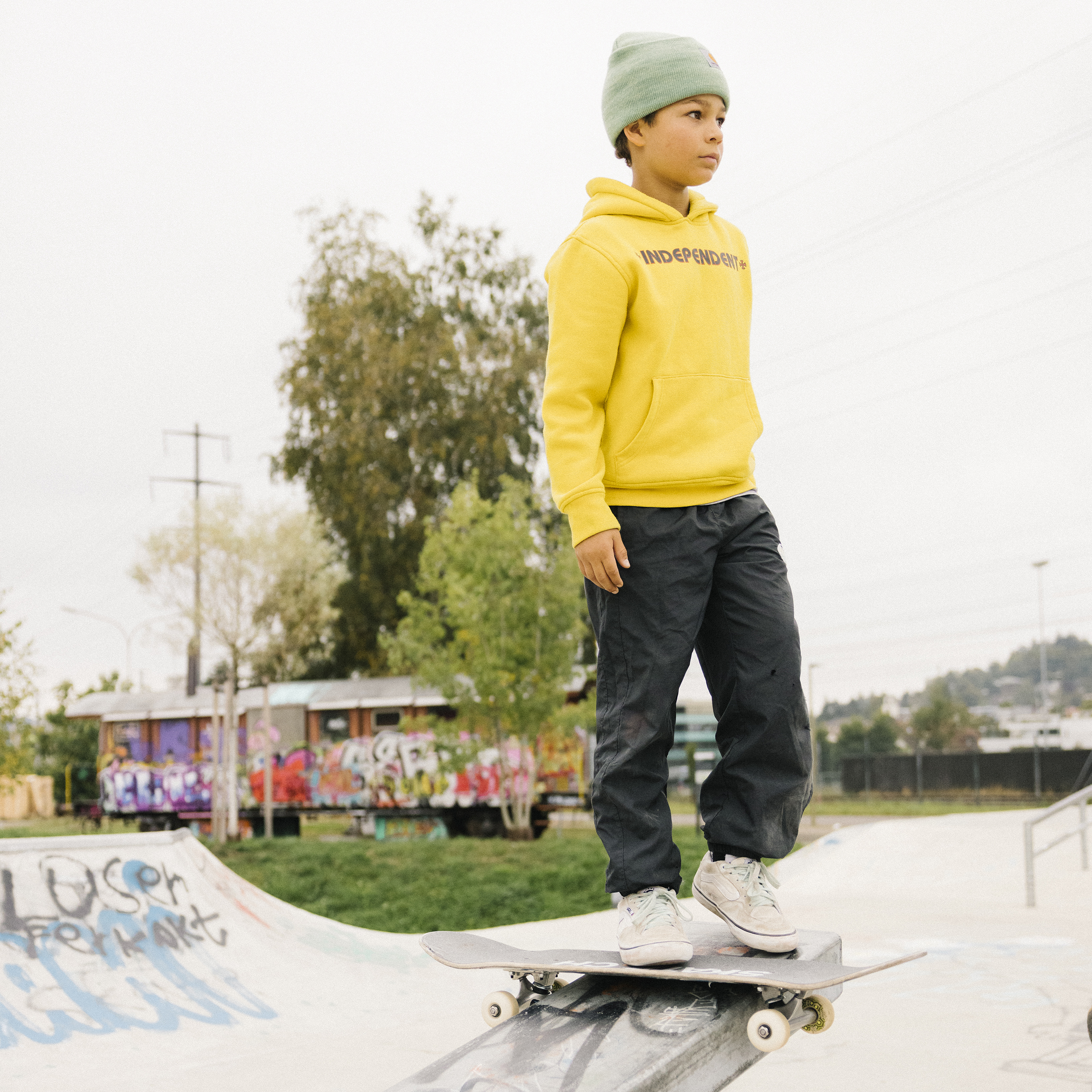 Un ragazzo è in piedi su una barra da grind con il suo skateboard e guarda con fiducia in lontananza.