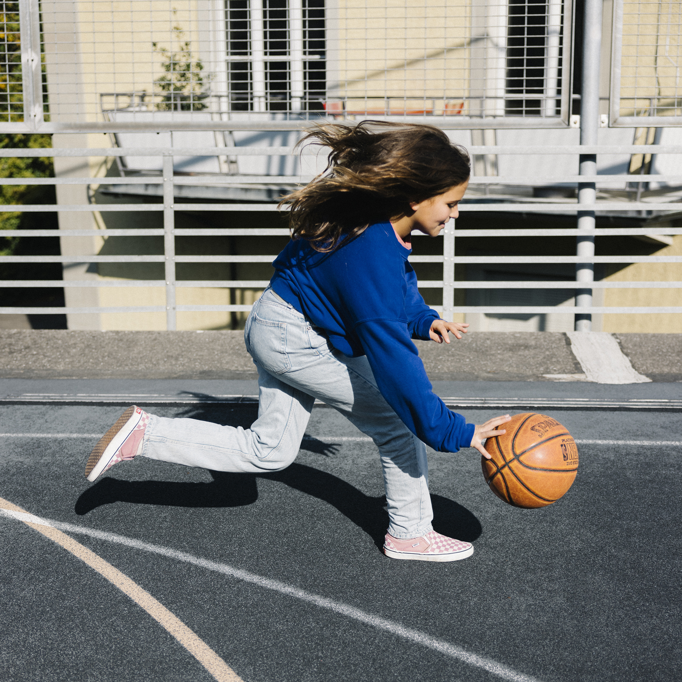Una ragazza palleggia una palla da basket sul terreno mentre corre.
