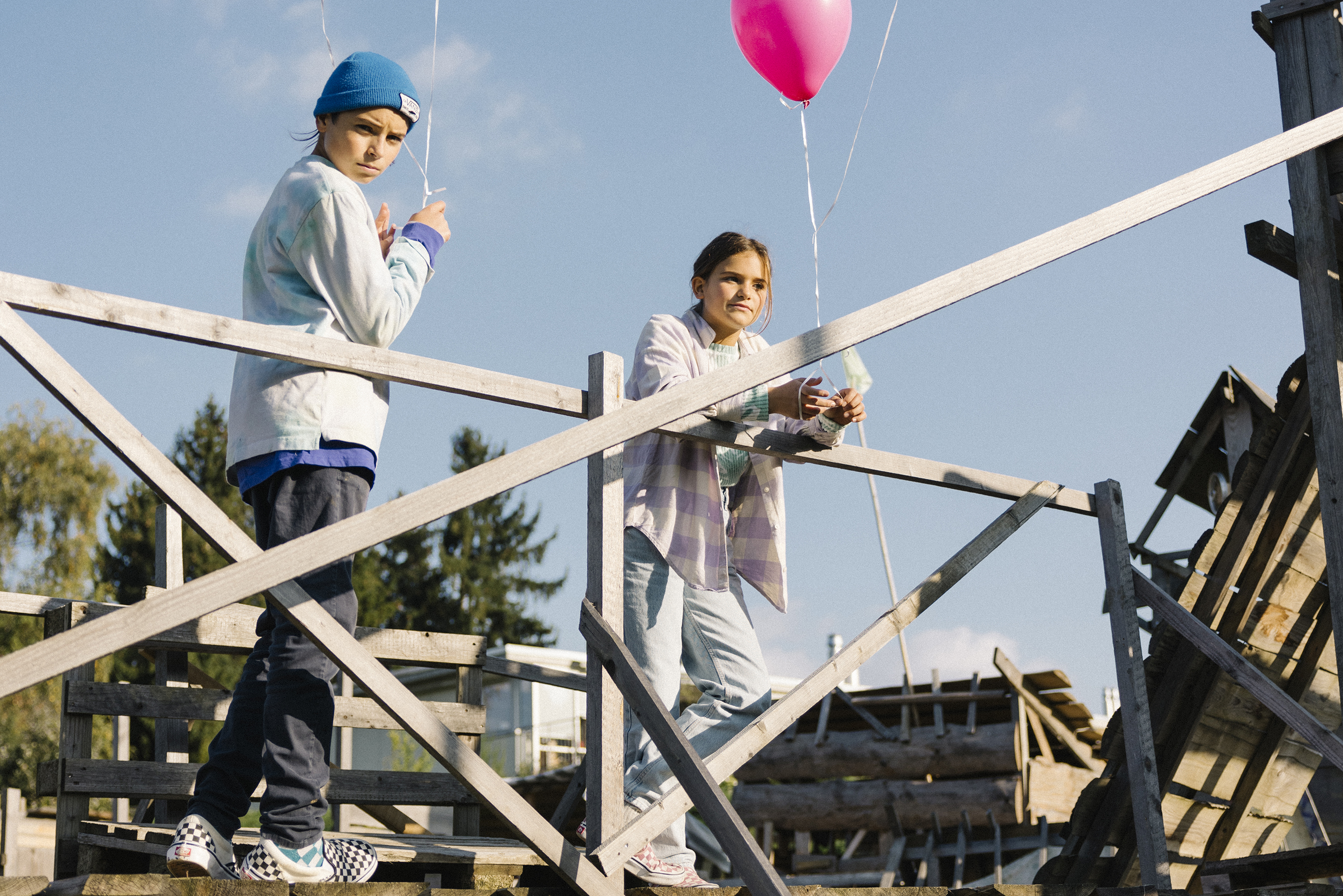 Two young people stand against a railing with concentrated gazes while holding two balloons per person