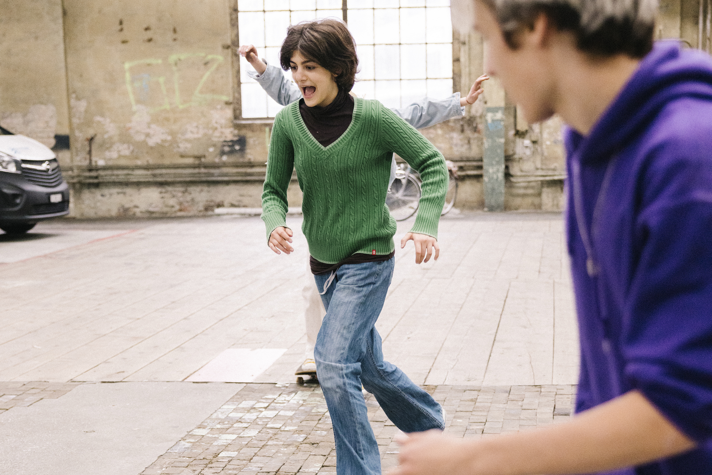 A teenager runs laughing towards her skateboard lying on the ground.